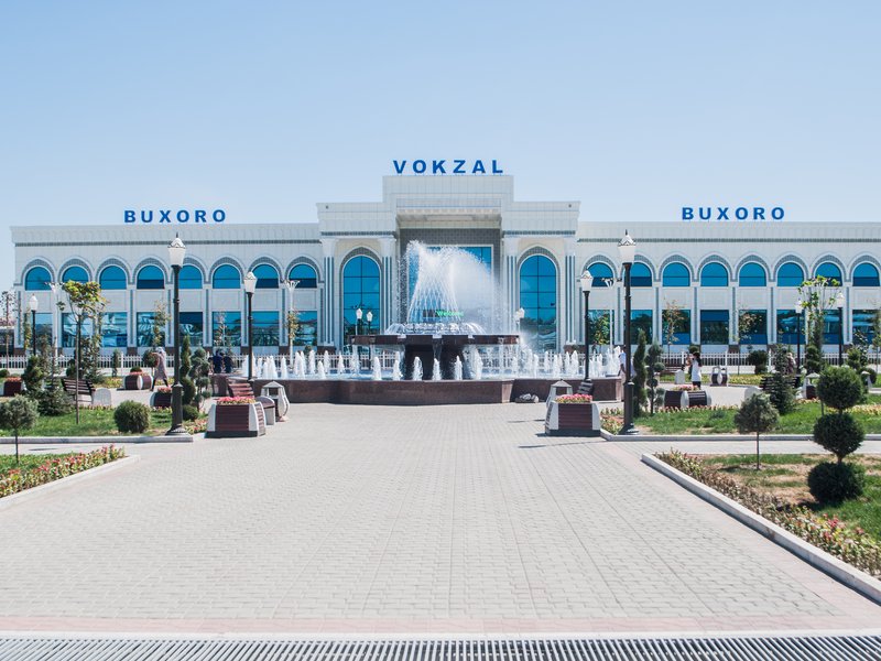 Bukhara Railway Station daytime facade in Kogon with BUXORO VOKZAL signage and plaza fountain