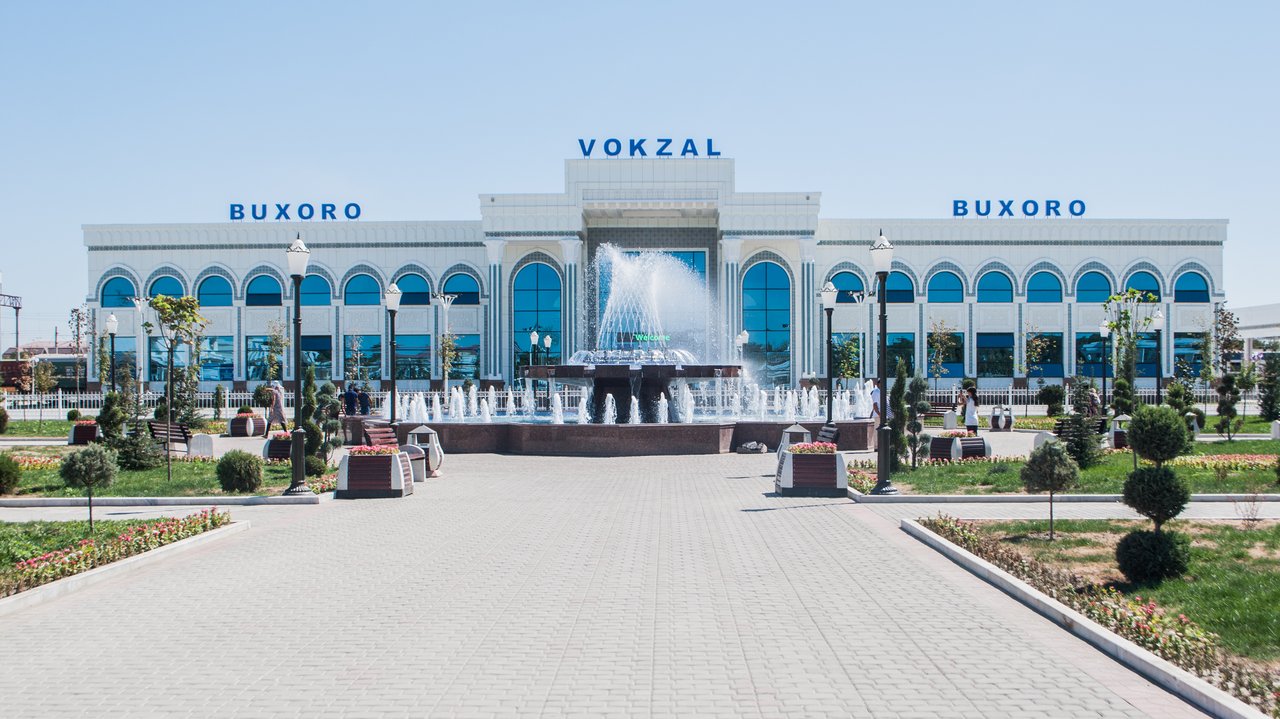 Bukhara Railway Station daytime facade in Kogon with BUXORO VOKZAL signage and plaza fountain