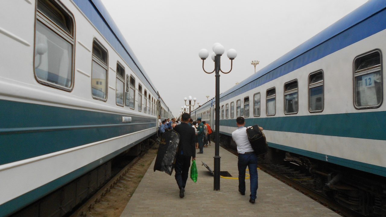 Passengers with luggage boarding a long-distance train between platforms at Nukus station